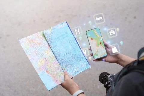 Cropped hands holding paper map and smartphone with digital navigation icons for Stock Photos