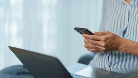 Cropped hands using smartphone while working on laptop at home 库存照片