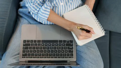 Cropped hands writing in notebook and using laptop on couch for remote work 스톡 사진