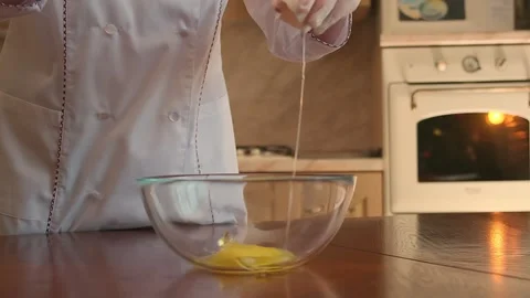 Cropped image of a cute pastry chef girl breaking an egg into a bowl and 库存影片 146680420