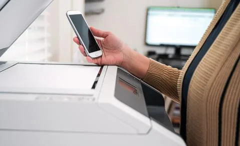 Cropped image of female holding cellphone with printer to print the document. Stock Photos