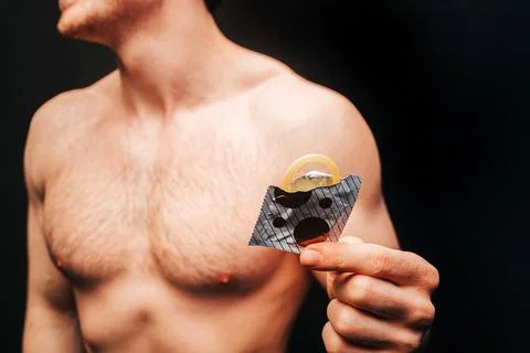 Cropped image of man holding opened package with condom in hand. Obscure face of Stock Photos