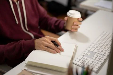 Cropped image of a man sitting in front of a computer, taking notes in a bo.. Stock Photos