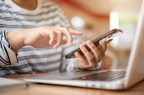 A cropped image of a woman multitasking, using her smartphone while working.. Stock Photos