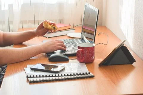 Cropped man working from from home. Using computer and eating donuts. Stock Photos