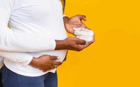 Cropped of pregnant couple holding baby shoes over yellow background Stock Photos