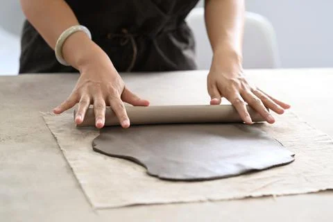 Cropped shot of ceramists using rolling pin for clay mass, making handicrafts at Stock Photos