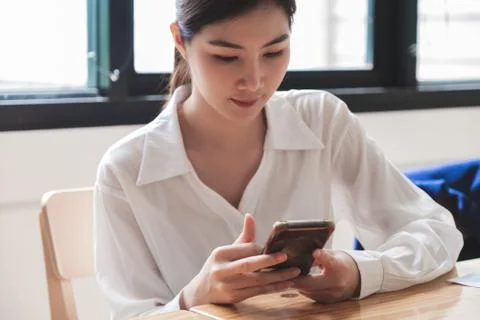 Cropped shot of charming asian female in white shirt using smart phone Stock Photos