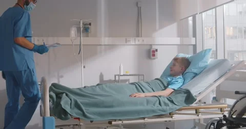 Cropped shot of doctor writing notes standing near hospital bed of sick boy Stock Footage 154149597