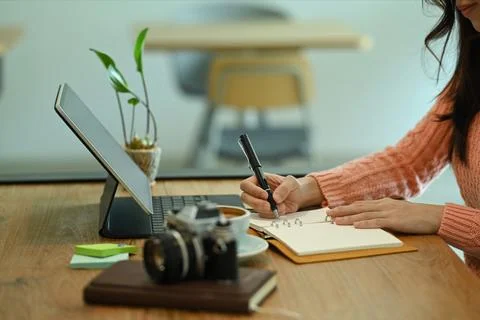 Cropped shot female using computer tablet and making notes on notebook. Stock Photos