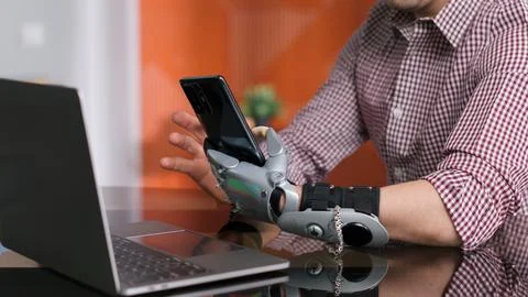 Cropped shot of man with bionic arm using smartphone sitting at desk in office Stock Photos