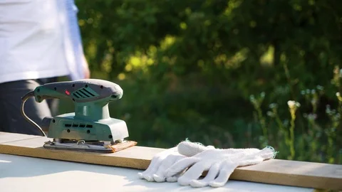 Cropped shot of man puts on gloves and sands wooden plank with electric machine Video stock 112890571