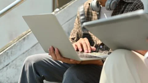 Cropped shot of students using laptop computer, sitting on stairs in front of a Stock Photos