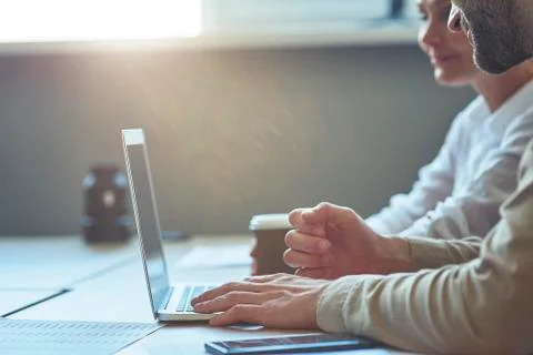 Cropped shot of two colleagues using laptop while sitting at desk in the modern Stock Photos