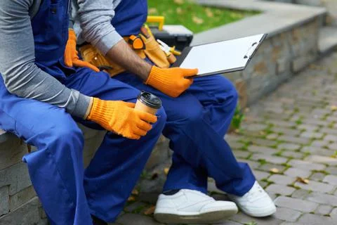 Cropped shot of two young workmen in uniform sitting outdoors having coffee Stock Photos
