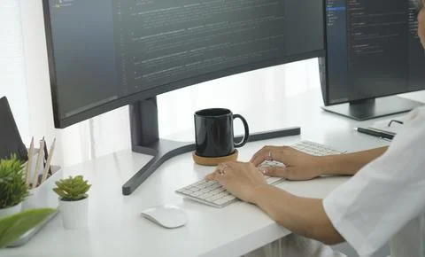 Cropped shot of young programmer writing program code with two monitors in .. 库存照片