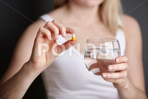 Cropped Shot Of Young Woman Holding Medicine Capsule And Glass Of Water