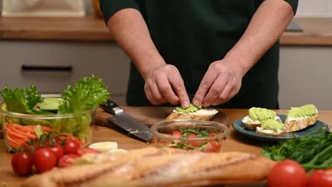 Cropped unrecognizable man in kitchen arranging avocado slices on bread, Stock Footage 331545752