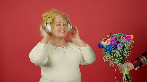 Cropped view of man presenting flowers to senior woman listening music in Vidéo 129413445