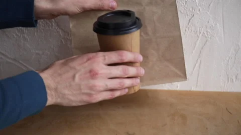 Cropped view of man putting paper bag and disposable cup on wooden surface Stock-Footage 132445237