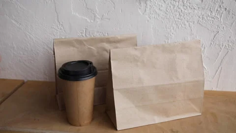Cropped view of man in taking paper bag and disposable cup from wooden surface 库存影片 132445162
