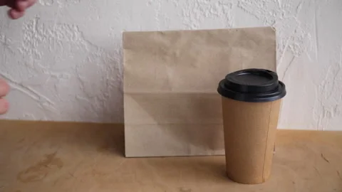 Cropped view of man taking paper bag and disposable cup from wooden surface 库存影片 132445609