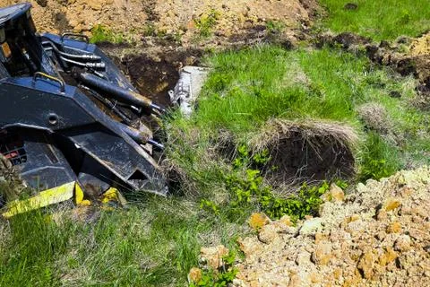 Cropped view of mini loader digging pit during earth works on grassy field Stock Photos