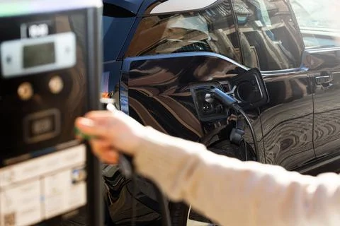 Cropped view of woman's hand using recharge city station to charge electric car. Stock Photos