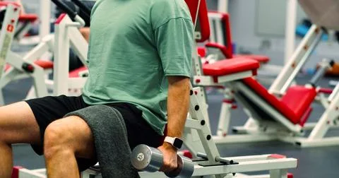 Cropped view of a young Caucasian man trains his bicep muscles with dumbbells in Stock Photos