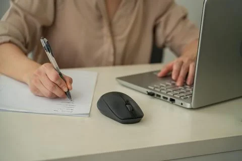 Cropped Woman Writing Notes While Using Laptop at Office Desk Stock Photos