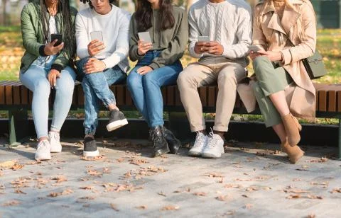Cropped of young friends using mobile phones, sitting on bench Stock Photos