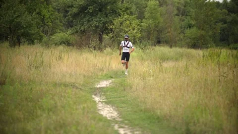 Cross-country runner training on grassy trail winding through lush meadow Stock Footage 313951352