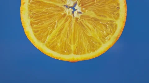A cross-cut orange slice is squeezing its juice in a macro shot with a blue Stock Footage 332081338