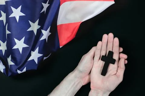 Cross in male hands against the background of the American flag Stock Photos