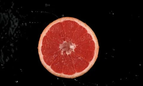 A cross-section of a ripe, red grapefruit is shown against a black background Stock Photos