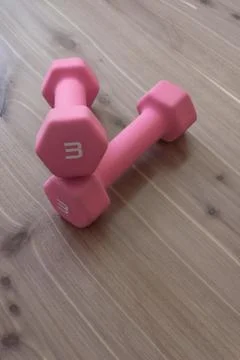 Cross stacked pair of hand weights, soft pink on neutral wood grain Stock Photos