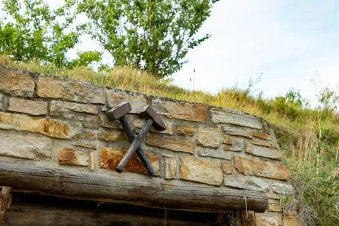Crossed mining hammers symbol on old stone wall above mine entrance. Stock Photos
