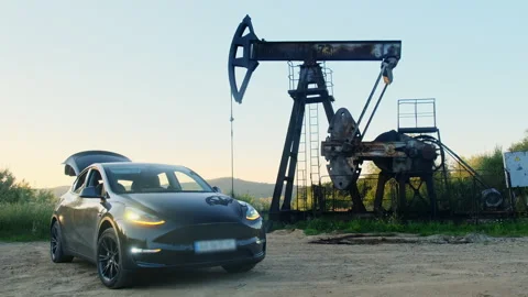 Crossover parks near rusty pumpjack as counterweight rotates Stock Footage 323886420