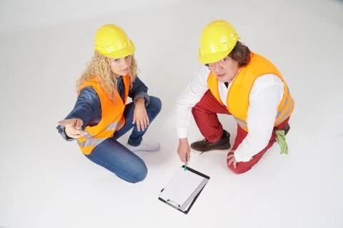 Crouched construction workers, a man and a blonde girl, on white background Stock Photos