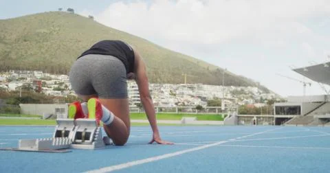 Crouching sprinter pushing off starting blocks on blue track, wearing black tank Stock Photos