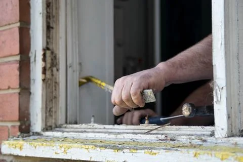 Crowbar being used to remove an old wooden window frame in brick wall Foto stock