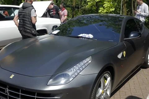 Crowd Admiring a Sleek Matte-Gray Ferrari FF Sports Car at a Lively Outdoor.. Stock Photos