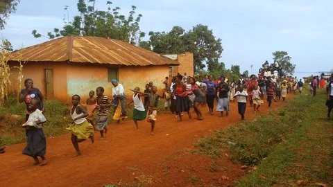 A crowd of Africans dancing and walking down a dirt road in a rural village Stock Footage 92654193