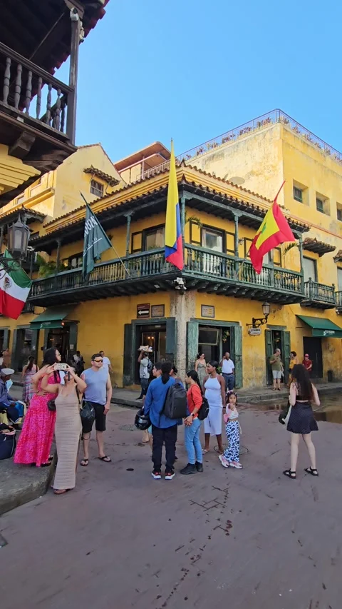 Crowd Beneath Yellow Balconied Corner With Flags, Cartagena, Colombia – Vertical Video stock 331499224