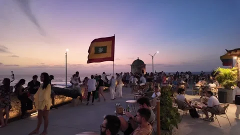 Crowd Gathering at Sunset Terrace Bar on Historic City Wall with Flag in Stock Footage 339963106