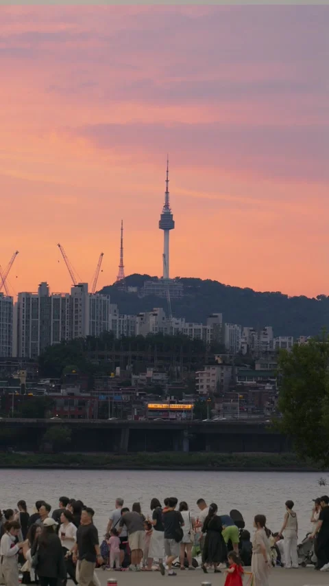Crowd Gathers at Han River as N Seoul Tower Rises Under Sunset Sky - vertical Stock Footage 340889067