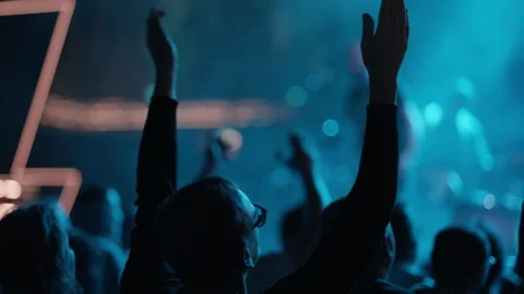 Crowd hands raised toward stage with performer silhouette in teal Stock Footage 334351875