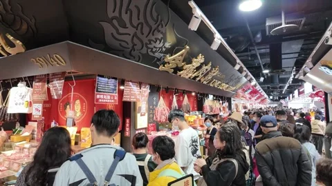 Crowd of people queuing at a food stall selling hanging sausages in a market Stock Footage 345998809
