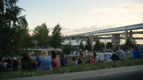 Crowd people sit on grass and relax against background city park in evening 4K. Stock Footage 114299476