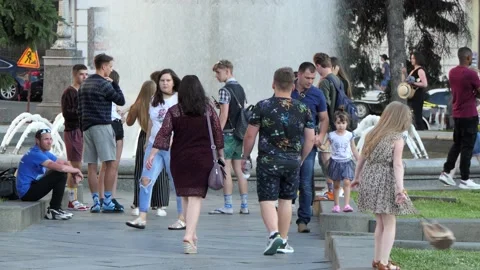 A crowd of people, townspeople walk, while away the time at the round fountain. Stock Footage 134464905